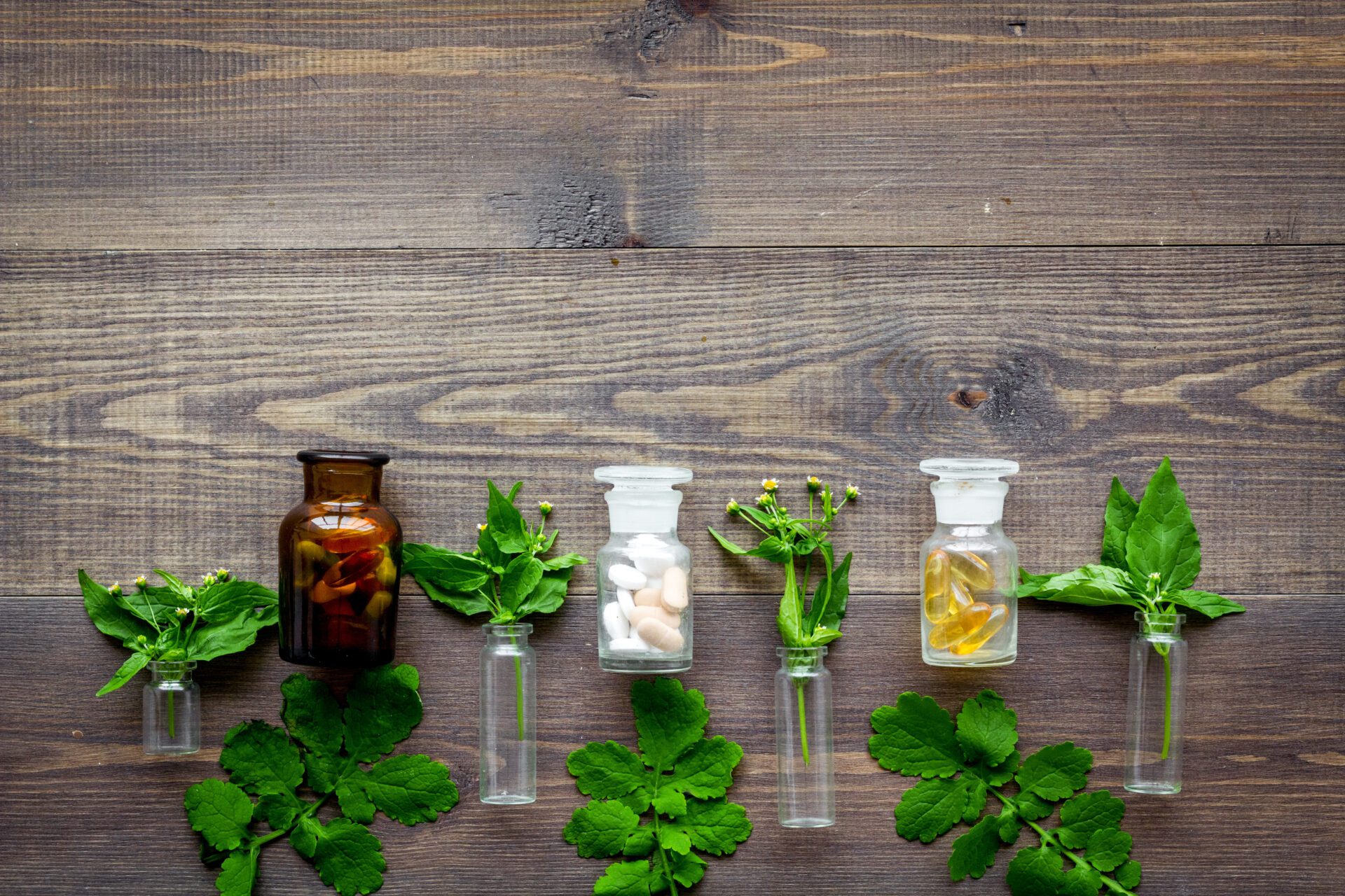 Herbal medicine pattern. Leaves, bottles and pills on wooden background top view copyspace